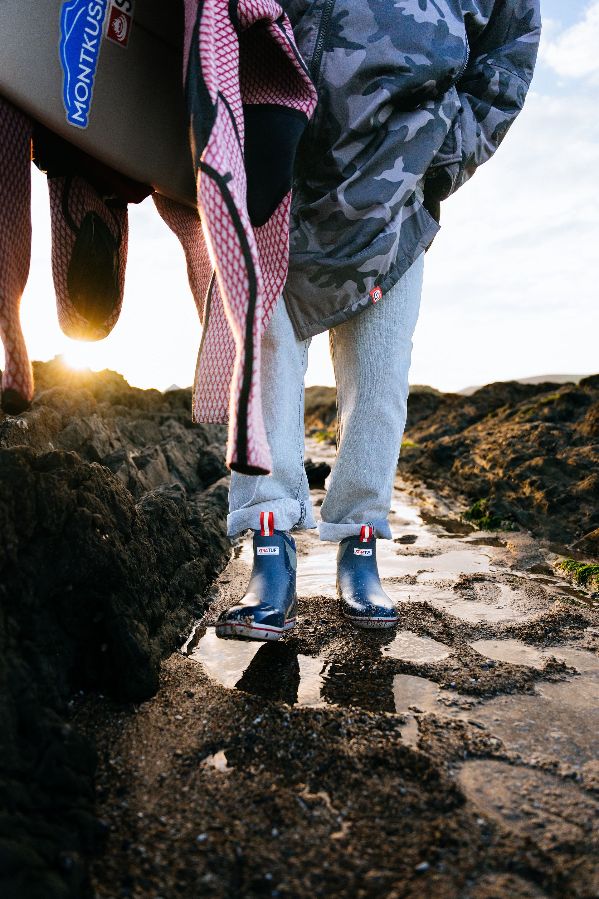 Person wearing blue rain boots on a rocky path with a sunset in the background