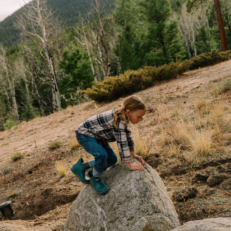 Child climbing a rock in a forested area