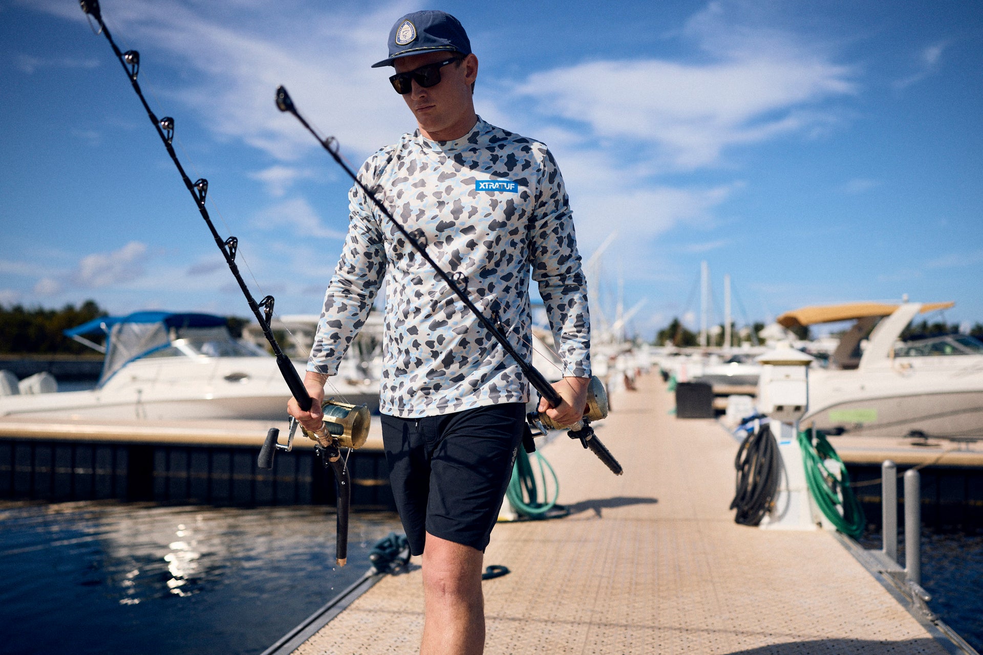 Man holding a fishing rod on a dock with boats in the background