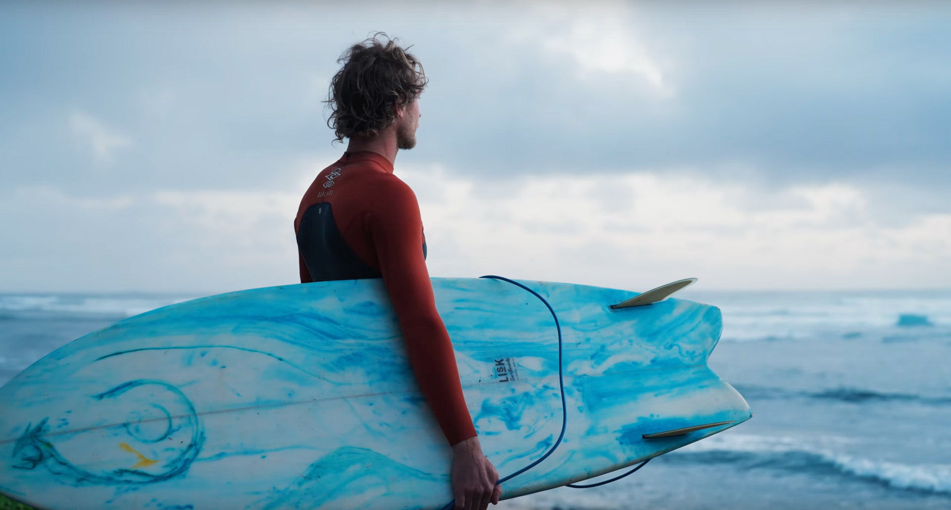 Person holding a blue surfboard with ocean and sky in the background