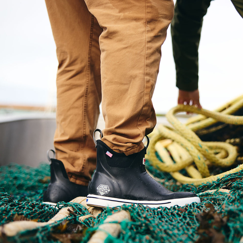 Person wearing black boots with white soles on a fishing net, standing on a boat.