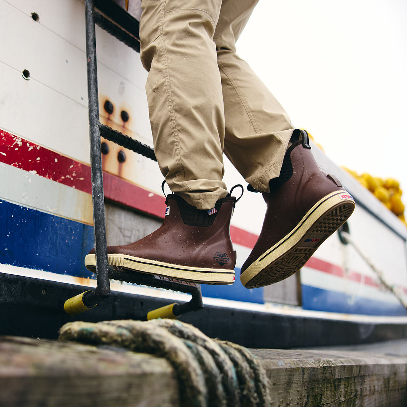 Person wearing brown boots with a visible brand logo, standing on a boat.