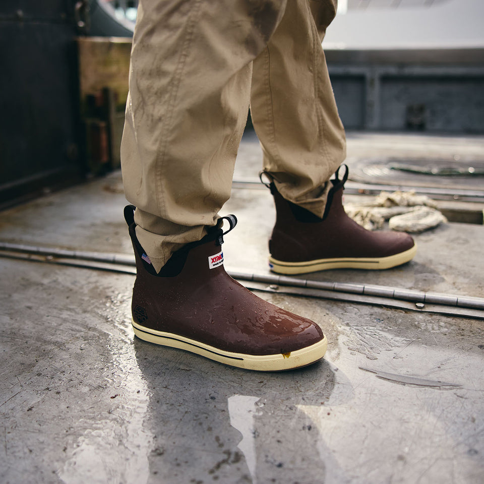 Brown ankle boots with yellow soles worn by a person on a concrete floor.