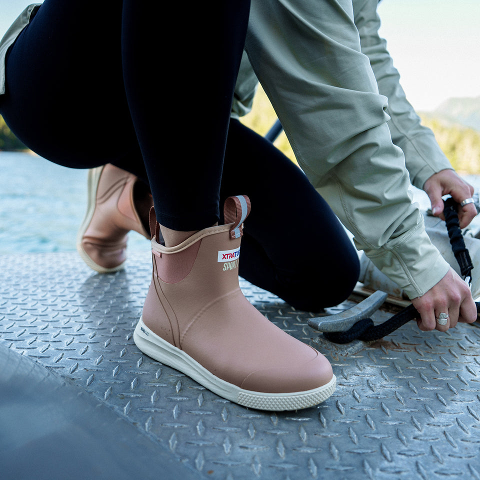 Person wearing pink rain boots with a visible brand logo on a textured surface.