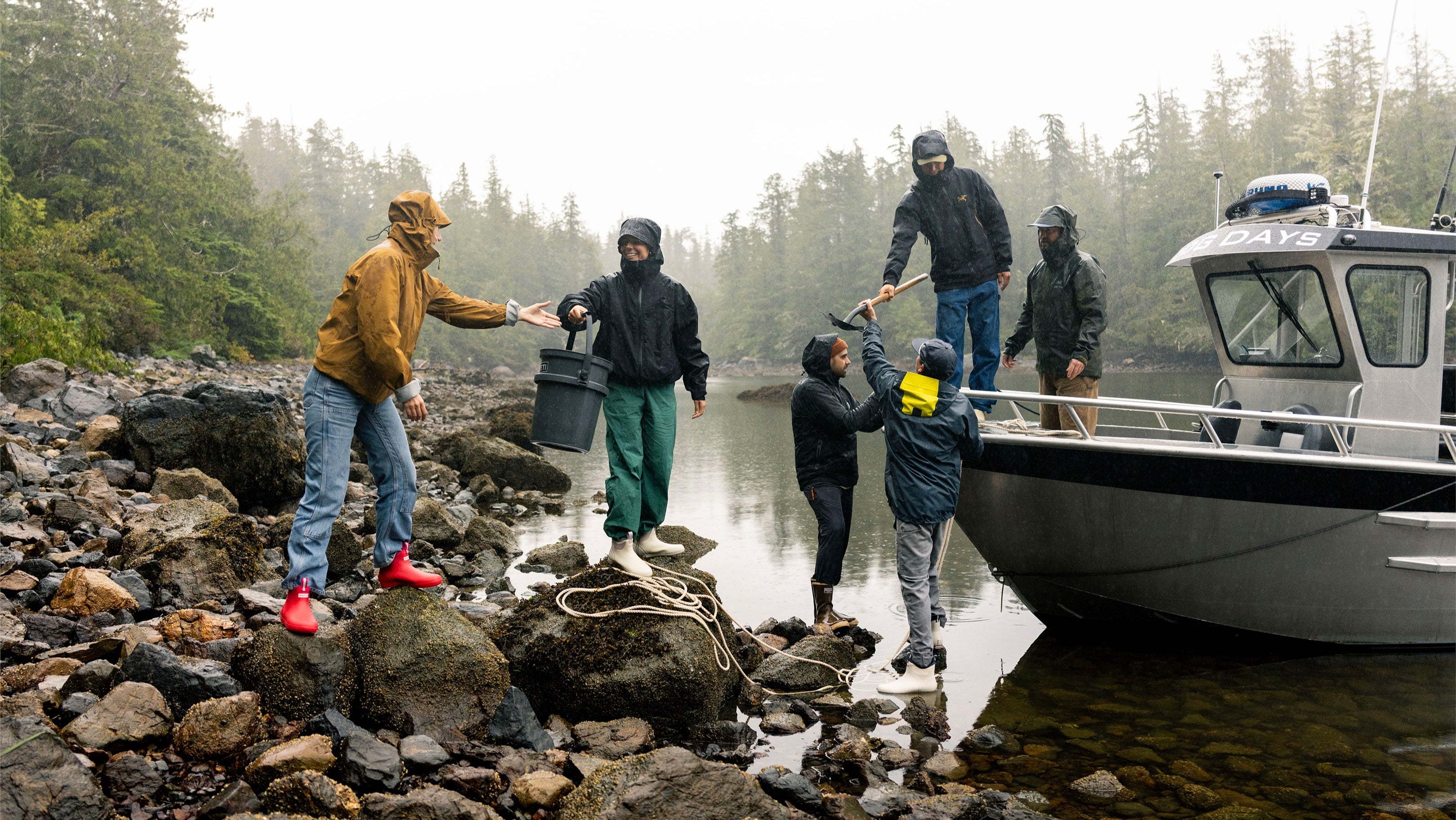 Group of people unloading a boat onto a rocky shore with trees in the background