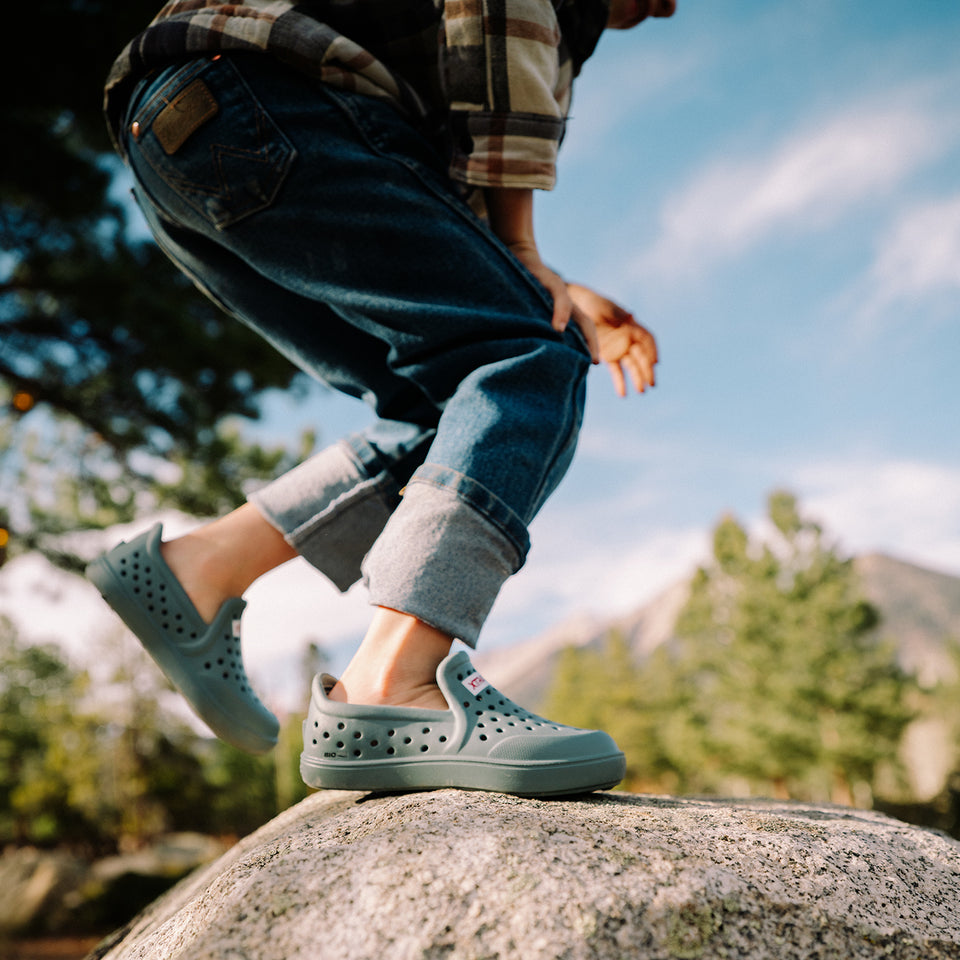 Person wearing light blue clogs standing on a rock with a natural background