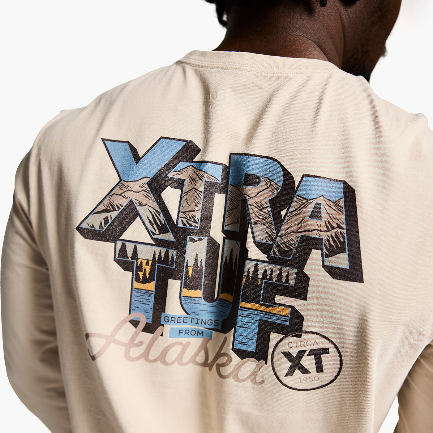 Person wearing a beige jacket with a graphic design on the back, featuring mountains and text.
