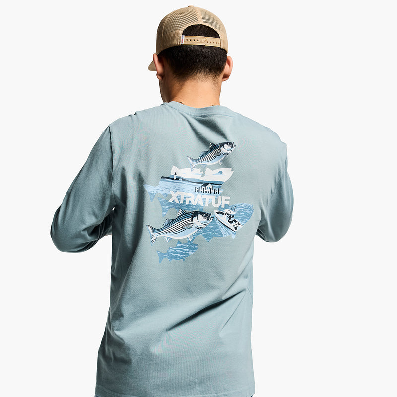 Man wearing a light blue long-sleeve shirt with a fish graphic on the back, standing against a white background.