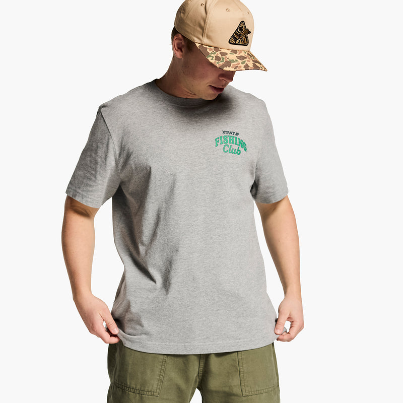 Man wearing a gray t-shirt with green text and a beige cap on a white background