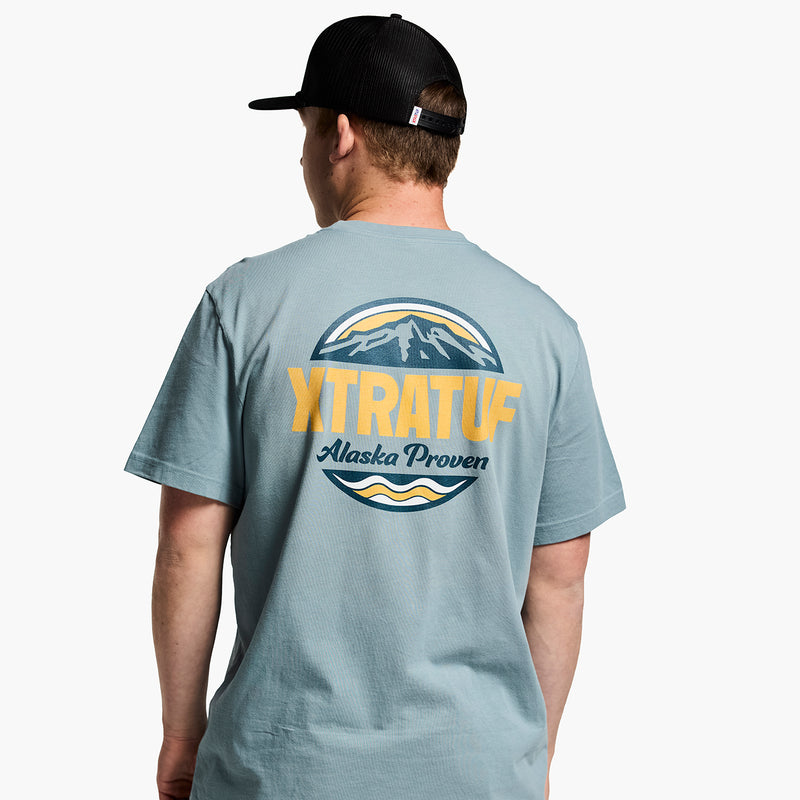 Person wearing a gray t-shirt with 'XTRATUF' logo and text on the back, white background