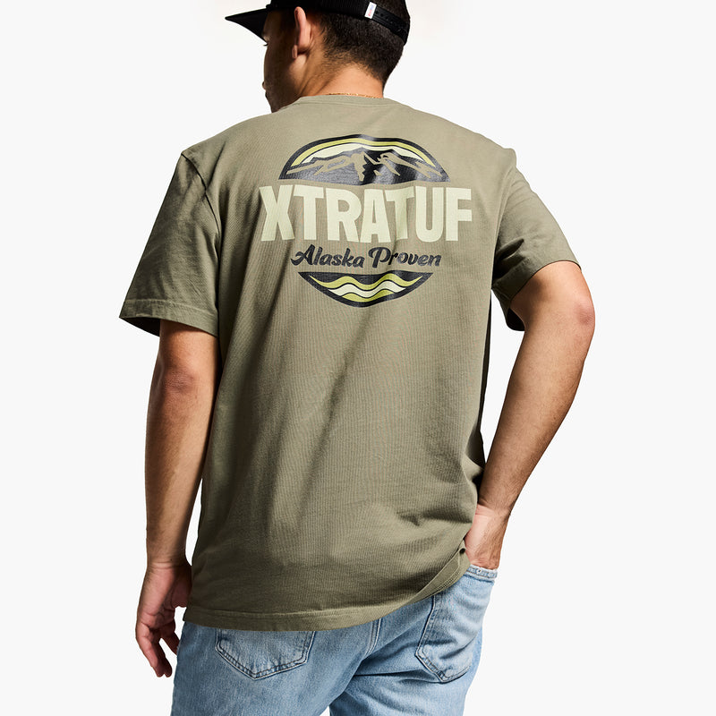 Person wearing a green t-shirt with 'XTRATUF' branding on the back, standing against a white background.