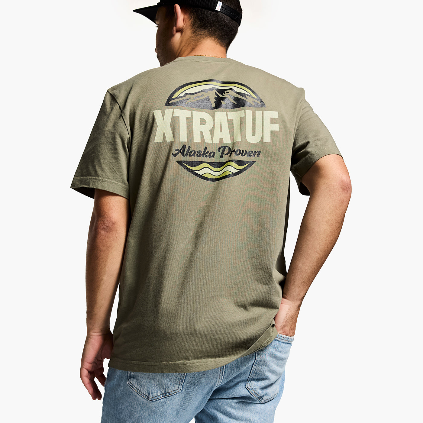 Person wearing a green t-shirt with 'XTRATUF' branding on the back, standing against a white background.