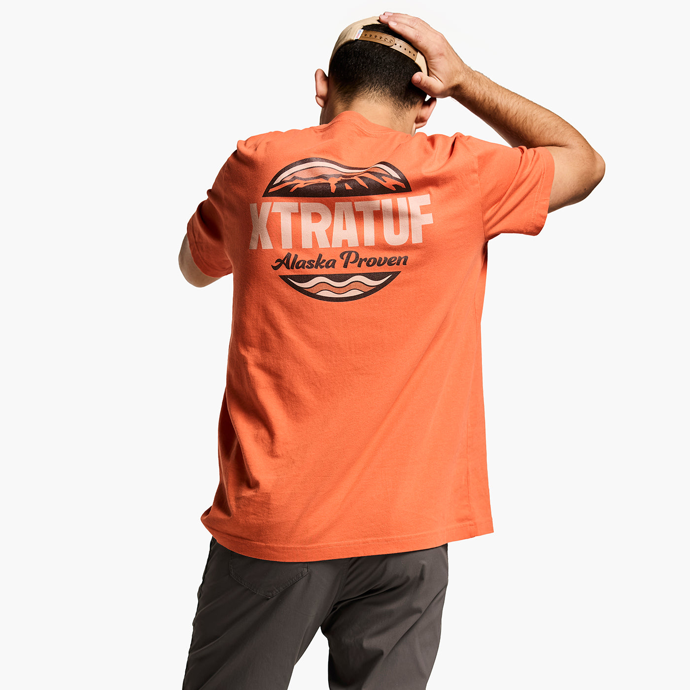 Person wearing an orange t-shirt with 'XTRATUF' branding on the back, wearing cap, standing against a white background.